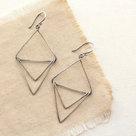 The oxidized silver triple triangle hoop earrings styled on tan linen