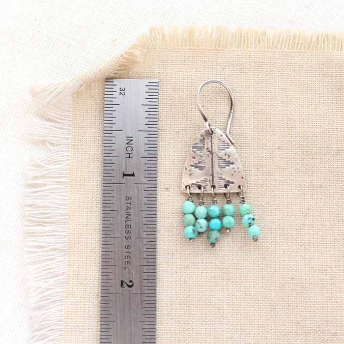 A pakal arch turquoise earring next to a ruler for size reference