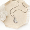 The pakal moon necklace styled on tan linen with a crystal