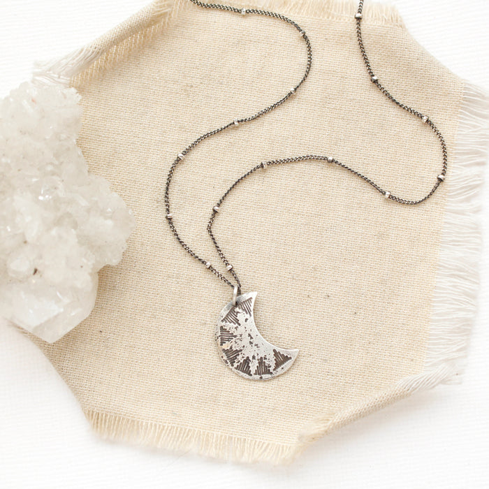 The pakal moon necklace styled on tan linen with a crystal