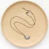 The pakal moon necklace styled on a tan plate to show the adjustable lobster clasp closure
