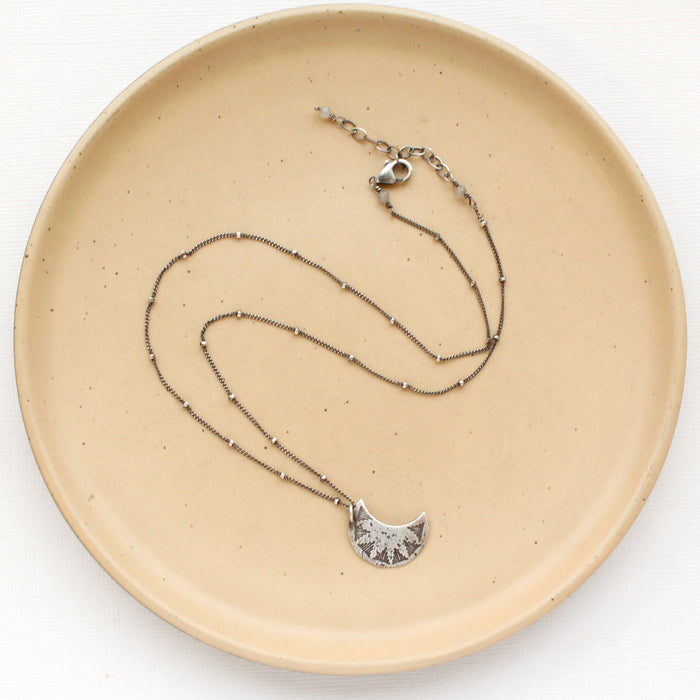 The pakal moon necklace styled on a tan plate to show the adjustable lobster clasp closure