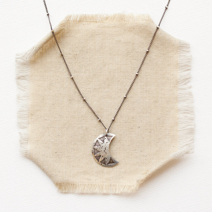 The pakal moon necklace styled on tan linen