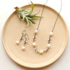 The oxidized pearl bud vine earrings styled on a tan plate with the matching necklace and an air plant