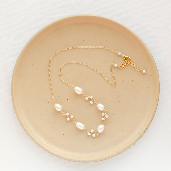 The gold wrapped pearl bud vine necklace styled on a tan plate to show the adjustable lobster clasp closure