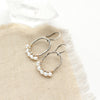 The pearl wrapped mixed metal hoop earrings styled on tan linen with a crystal