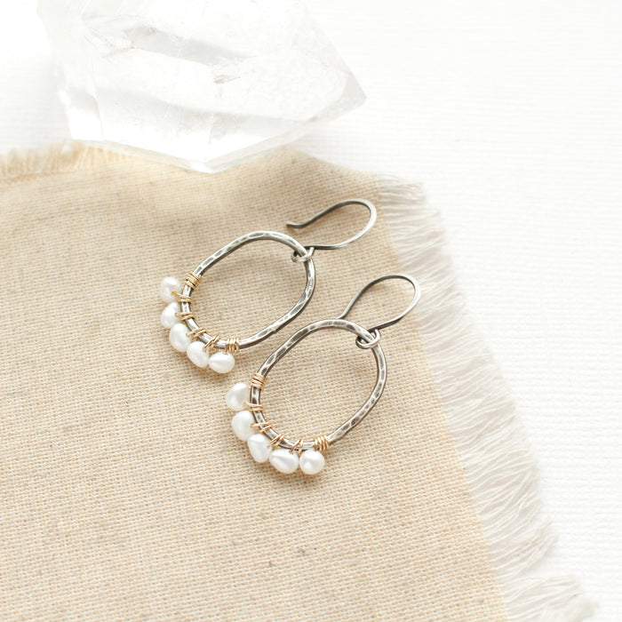 The pearl wrapped mixed metal hoop earrings styled on tan linen with a crystal