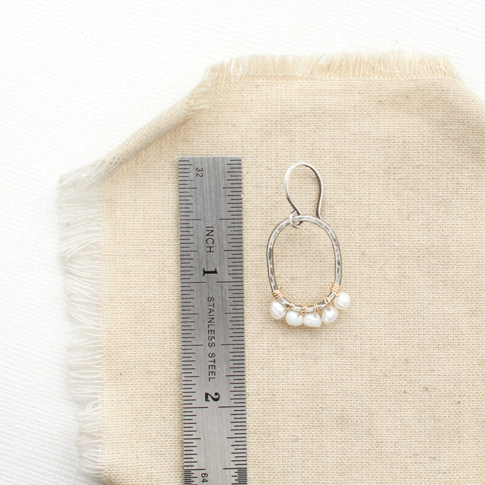 A pearl wrapped mixed metal hoop earring next to a ruler for size reference