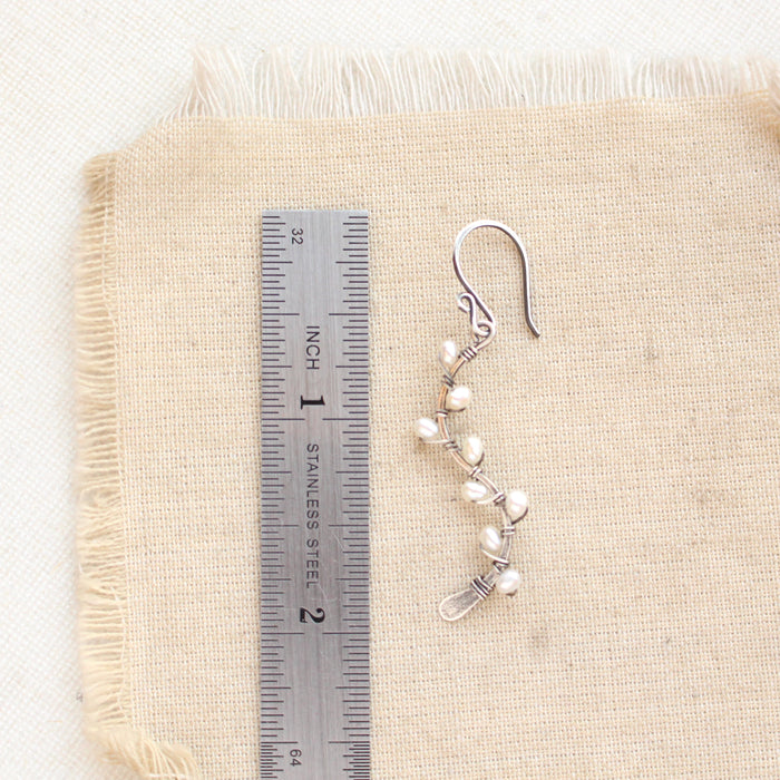 A pearl wrapped oxidized silver vine earring next to a ruler for size reference
