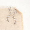 The pearl wrapped oxidized silver vine earrings styled on tan linen
