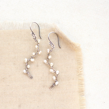 The pearl wrapped oxidized silver vine earrings styled on tan linen