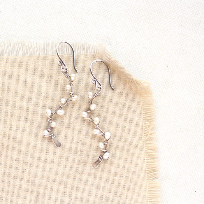 The pearl wrapped oxidized silver vine earrings styled on tan linen