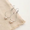 The elegant pearl wrapped teardrop mixed metal hoop earrings styled on tan linen