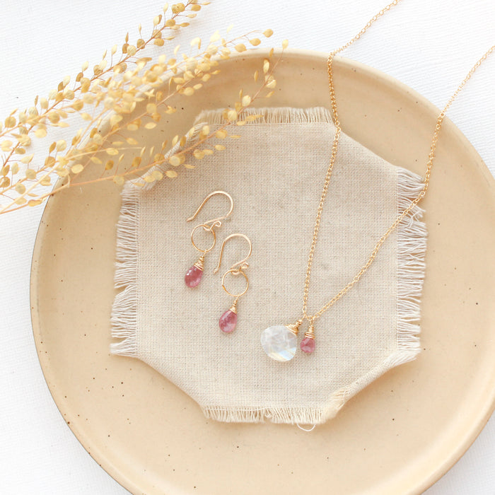 The pink sapphire and moonstone charm necklace styled on a tan plate with the matching earrings
