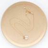 The pink sapphire and moonstone charm necklace styled on a tan plate to show the adjustable lobster clasp closure