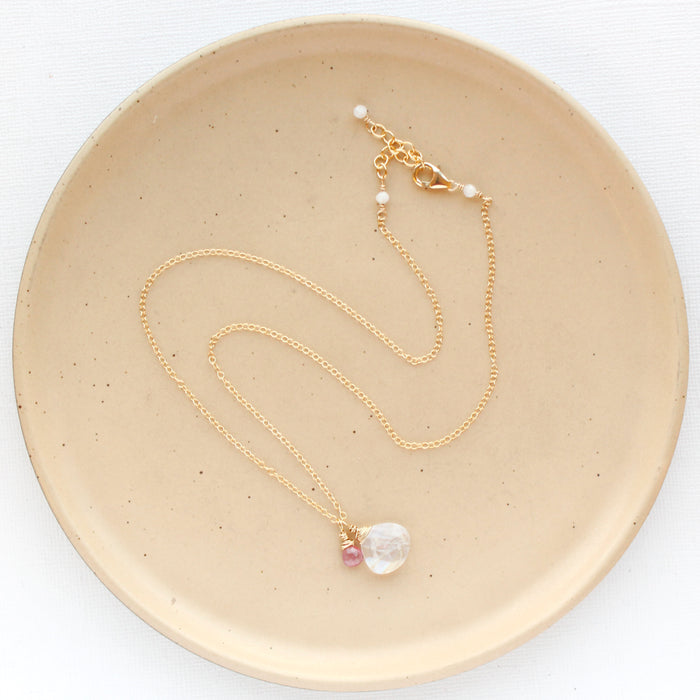 The pink sapphire and moonstone charm necklace styled on a tan plate to show the adjustable lobster clasp closure