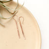 The rose gold beaded bar earrings styled on a tan plate with an air plant
