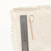A rose gold beaded bar earring next to a ruler for size reference