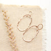 The rose gold organic hoop earrings styled on tan linen with dried grass