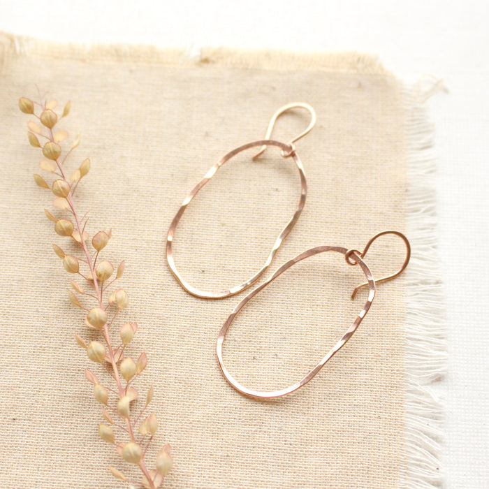 The rose gold organic hoop earrings styled on tan linen with dried grass