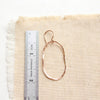 A rose gold organic hoop earring next to a ruler for size reference