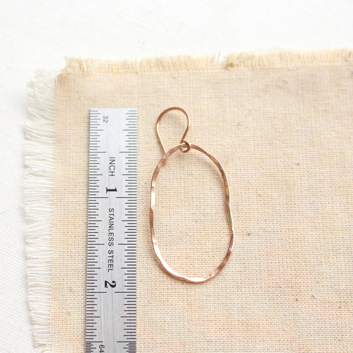 A rose gold organic hoop earring next to a ruler for size reference