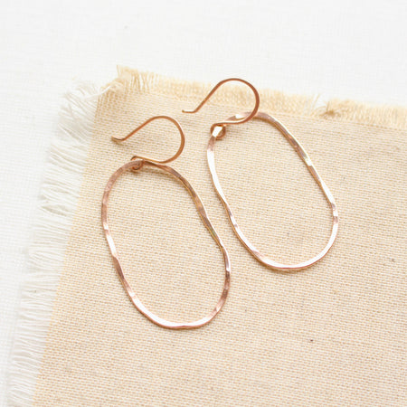 The rose gold organic hoop earrings styled on tan linen
