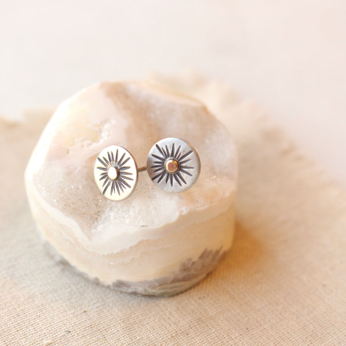 The rustic sun post earrings styled on a rock with tan linen