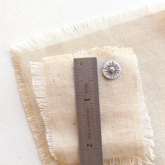 A rustic sun post earring next to a ruler for size reference