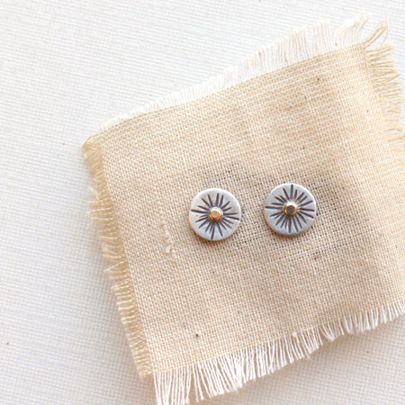 The rustic sun post earrings styled on tan linen