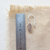 A stamped silver feather lobe hugger next to a ruler for size reference