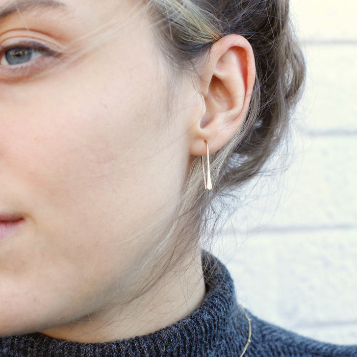 The gold hook earrings being worn in an ear