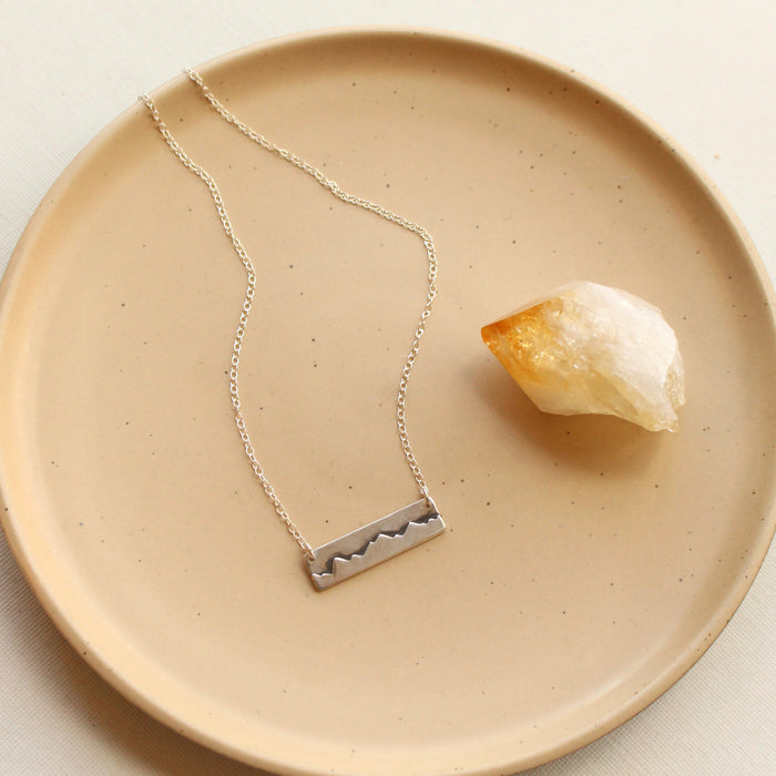 The layered silver mountain bar necklace styled on a tan plate with a crystal