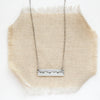 The oxidized silver mountain bar necklace styled on tan linen