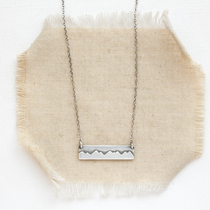 The oxidized silver mountain bar necklace styled on tan linen