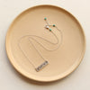 The silver layered mountain bar necklace styled on a tan plate to show the adjustable lobster clasp closure