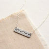 The layered silver mountain bar necklace styled on tan linen