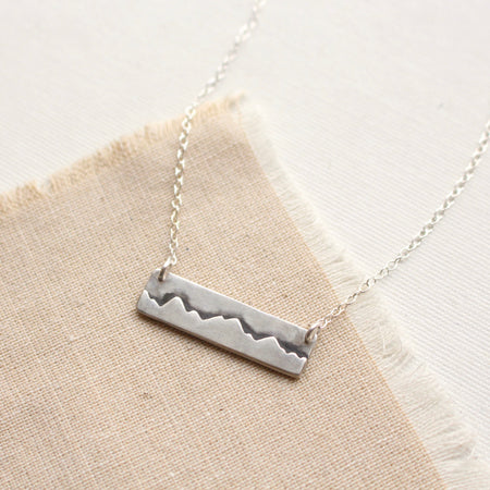The layered silver mountain bar necklace styled on tan linen