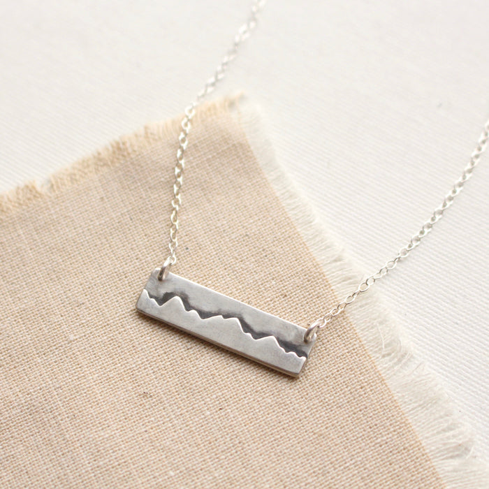 The layered silver mountain bar necklace styled on tan linen