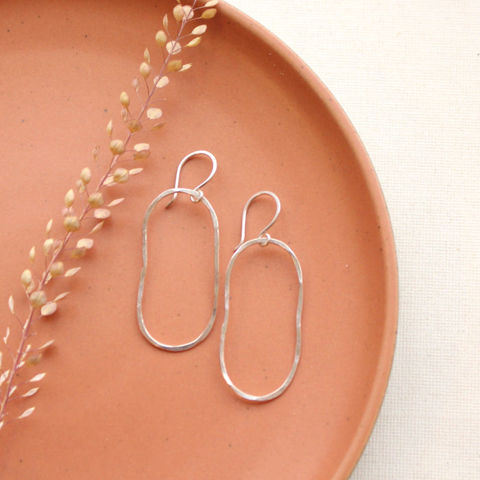 The silver organic hoop earrings styled on an orange plate with dried grass