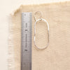A silver organic hoop earring next to a ruler for size reference