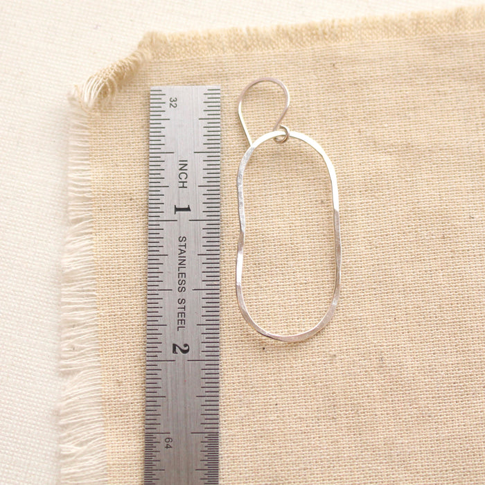 A silver organic hoop earring next to a ruler for size reference