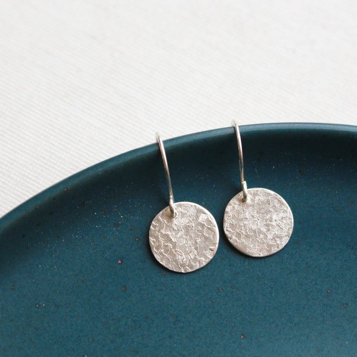 The silver raw silk disc earrings styled on a blue plate