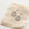 The silver raw silk disc earrings styled on tan linen