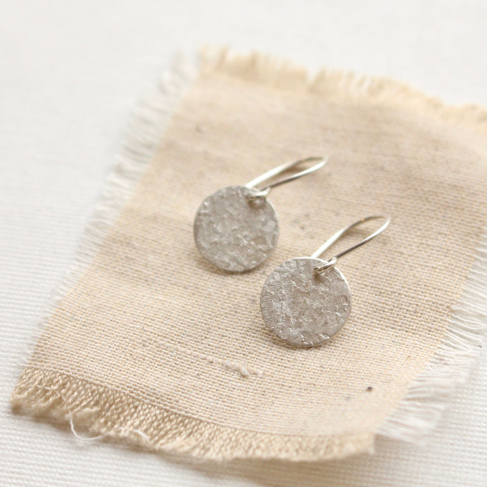 The silver raw silk disc earrings styled on tan linen