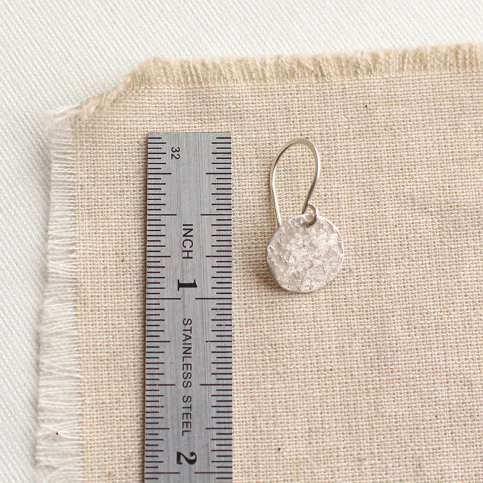 A silver raw silk disc earring next to a ruler for size reference