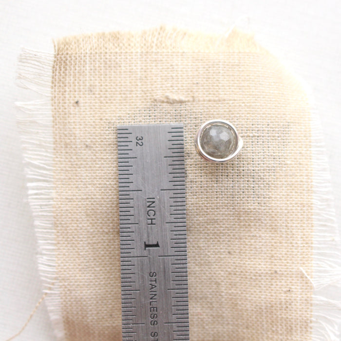 A silver wrapped labradorite post earring next to a ruler for size reference