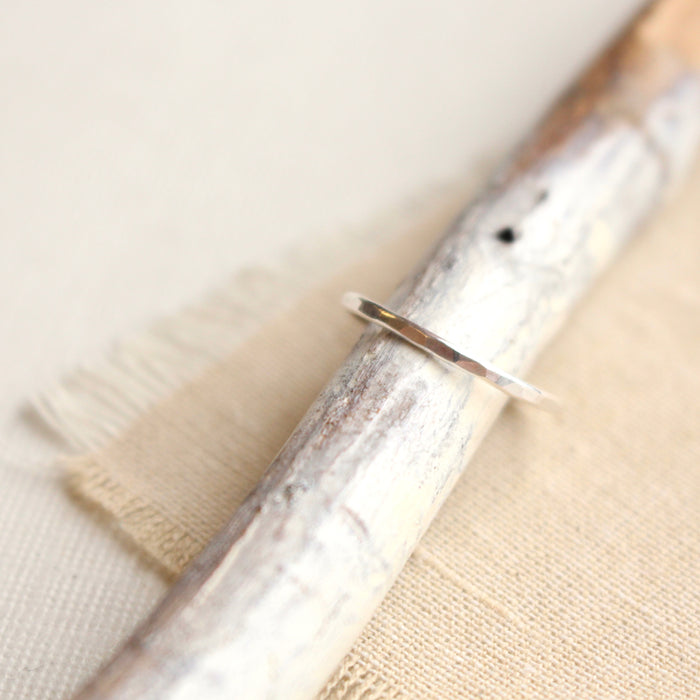 The skinny hammered silver stacking ring styled on a white stick with tan linen