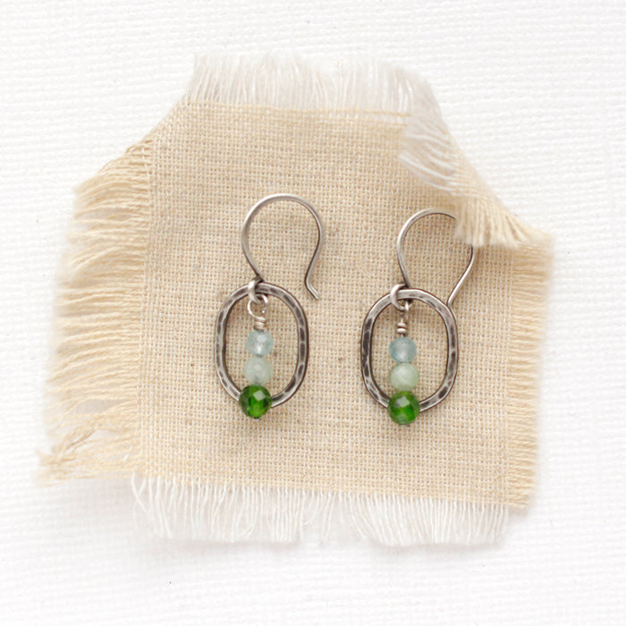 The stacked green chrome diopside, green apatite, and blue apatite mini hoop earrings styled on tan linen