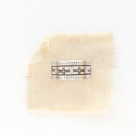 The stamped linear and cross band ring is styled on tan linen